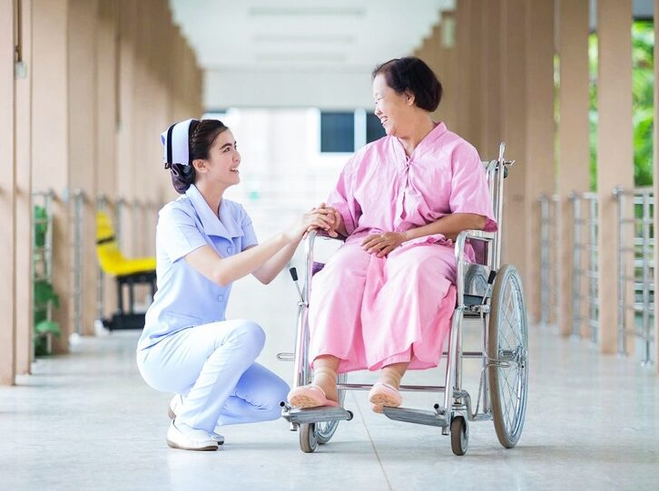 A nurse is holding the hand of an elderly woman in a wheelchair.